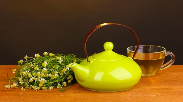 Bule e xícara com chá de camomila na mesa de madeira no fundo marrom — Fotografia de Stock