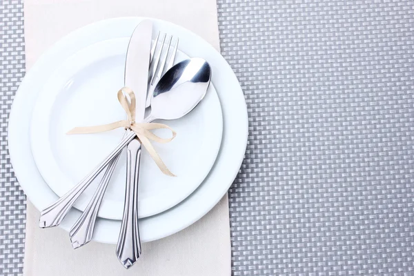 Platos blancos vacíos con tenedor, cuchara y cuchillo atados con una cinta sobre un mantel gris —  Fotos de Stock