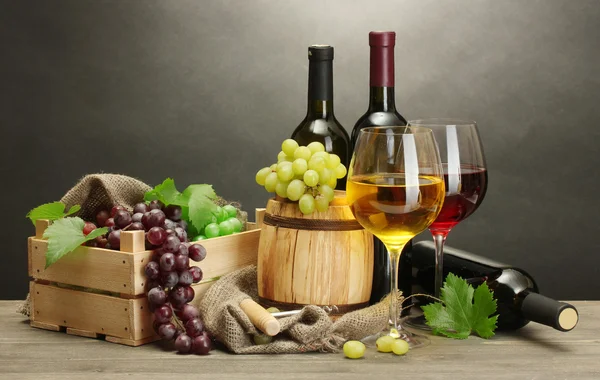 Tonneau, bouteilles et verres de vin et raisins mûrs sur table en bois sur fond gris — Photo