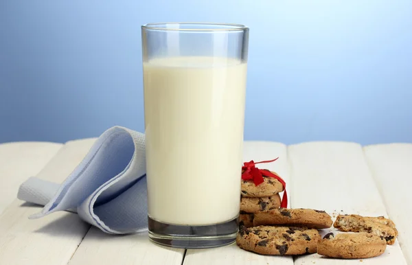Vaso de leche y galletas de chispas de chocolate con cinta roja en la mesa de madera sobre fondo azul —  Fotos de Stock