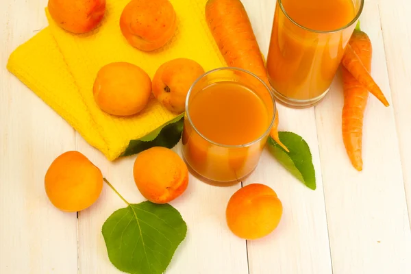 Gläser mit Karotten und Aprikosensaft auf weißem Holztisch — Stockfoto