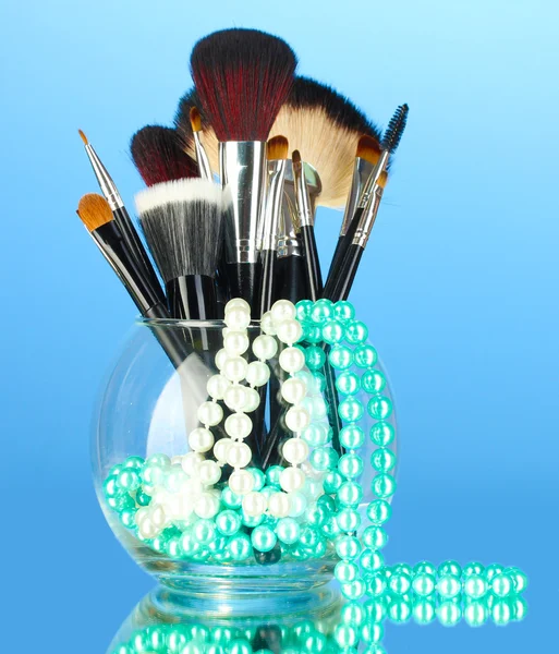 Make-up-Pinsel in einer Schüssel mit Perlenkette auf blauem Hintergrund — Stockfoto