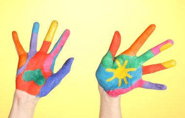 Brightly colored hands on yellow background close-up