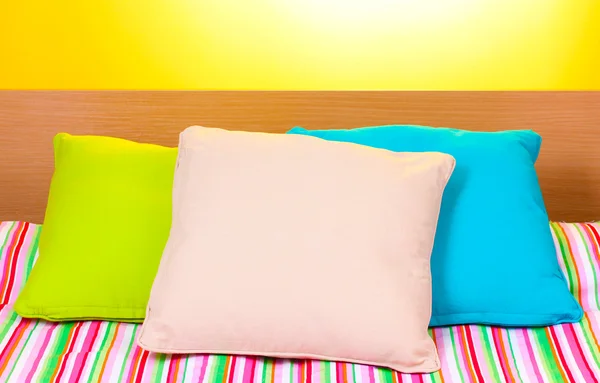 Almofadas brilhantes na cama no fundo amarelo — Fotografia de Stock