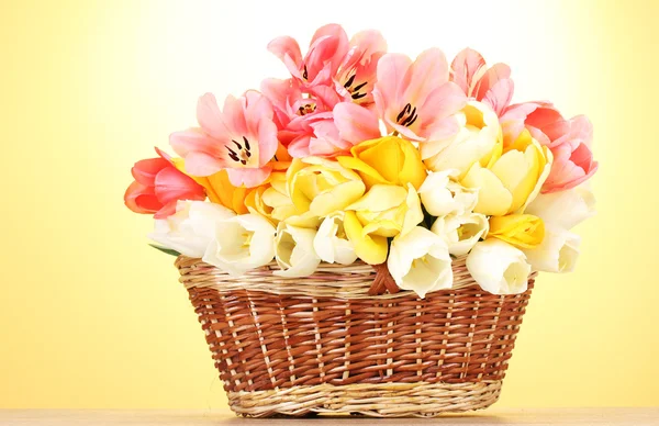 Schöne Tulpen im Korb auf Holztisch auf gelbem Hintergrund — Stockfoto