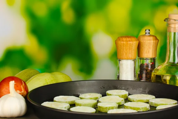 Нарізаний кабачок на сковороді на дерев'яному столі на зеленому фоні крупним планом — стокове фото