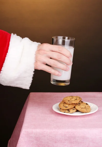 stock image Santa Claus hand holding glass of milk on brown background