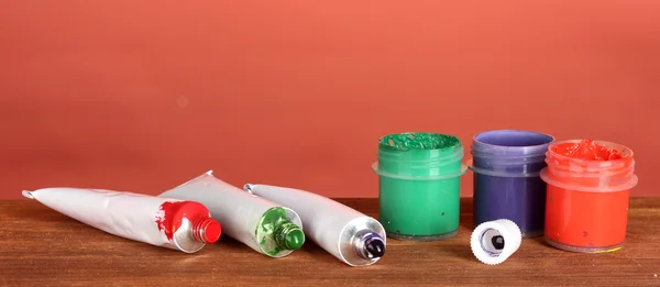 Tubos com aquarelas coloridas e frascos com guache na mesa de madeira sobre fundo brilhante — Fotografia de Stock