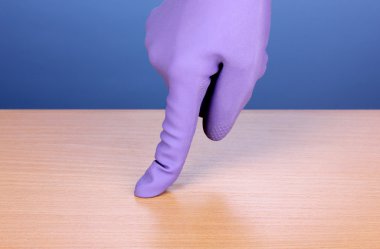 Hand in color cleaning glove holding finger over surface of wooden table on blue background clipart