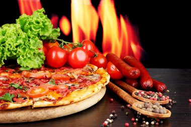 güzel pizza, salam, domates ve baharatlar alev arka plan üzerinde ahşap tablo