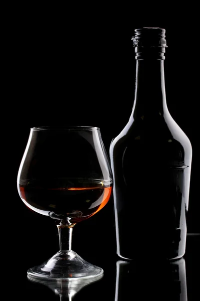 Glas brandy en fles op zwarte achtergrond — Stockfoto