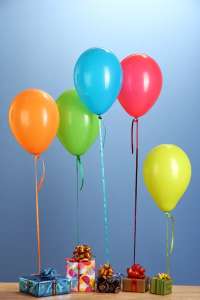 Färgglada ballonger håller en gåvor på ett träbord på blå bakgrund — Stockfoto