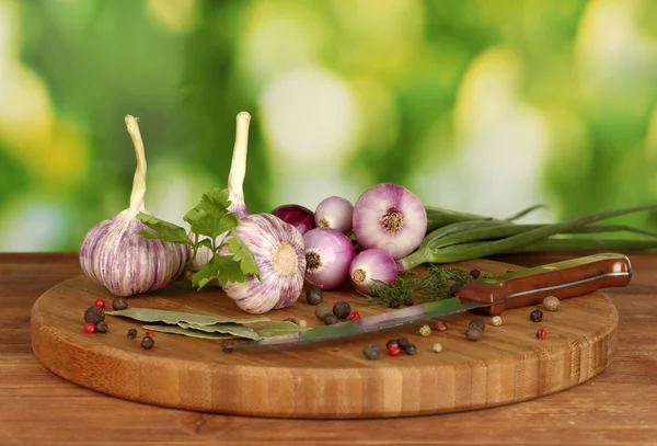 Young garlic and onion on cutting board with greenery, pepper and knife on wooden table on green — Stock Photo, Image