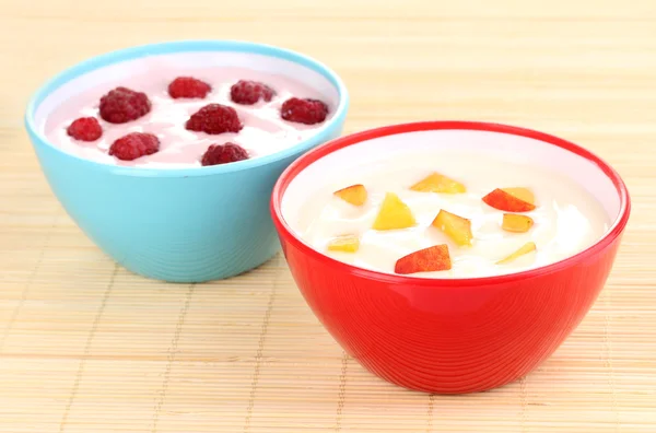 Йогурт с персиками и малиной в мисках на бамбуковом коврике — стоковое фото