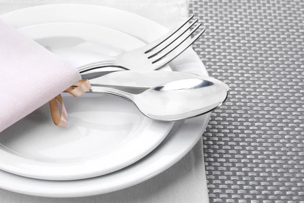 White empty plates with fork, spoon and knife tied with a ribbon on a grey tablecloth — Stock Photo, Image
