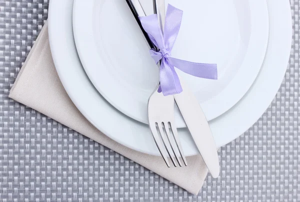 灰色のテーブル クロスにリボンで結ばフォークとナイフで白い空の皿 — ストック写真