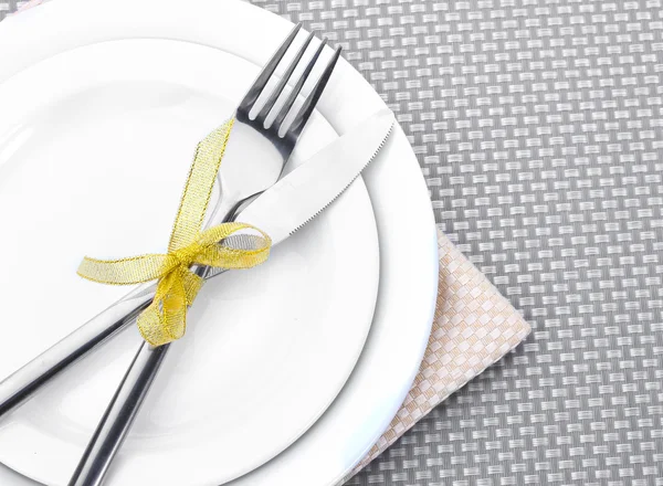 Piatti bianchi vuoti con forchetta e coltello legati con un nastro su una tovaglia grigia — Foto Stock