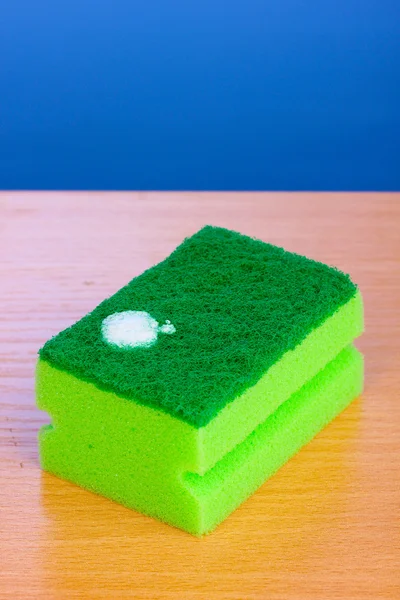 Sponge with dishwashing liquid on wooden table on blue background — Stock Photo, Image