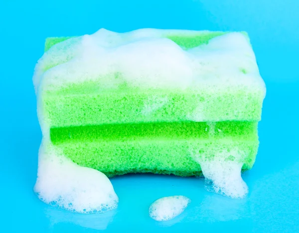 Esponja con espuma de líquido lavavajillas sobre fondo azul — Foto de Stock