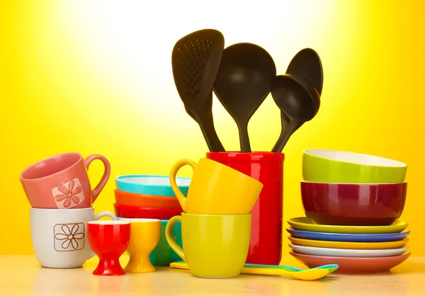 Ciotole vuote luminose, tazze e utensili da cucina su tavolo di legno su sfondo giallo — Foto Stock