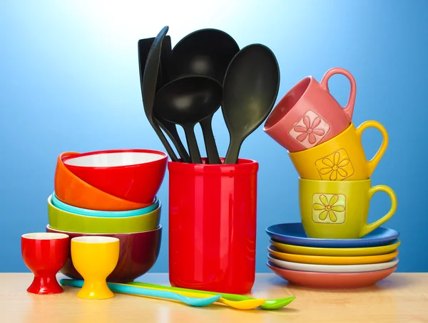 Яркие пустые миски, чашки и кухонные принадлежности на деревянном столе на синем фоне — стоковое фото