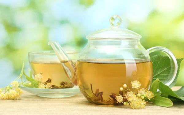Tetera y taza con té de tilo y flores en la mesa de madera en el jardín — Foto de Stock