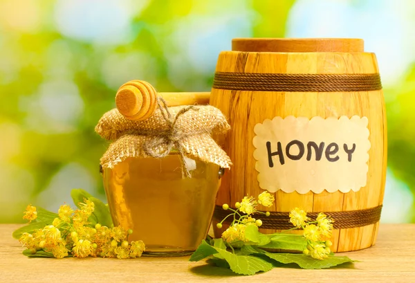 Βάζο και βαρέλι με linden μέλι και λουλούδια στο ξύλινο τραπέζι σε πράσινο φόντο — Φωτογραφία Αρχείου