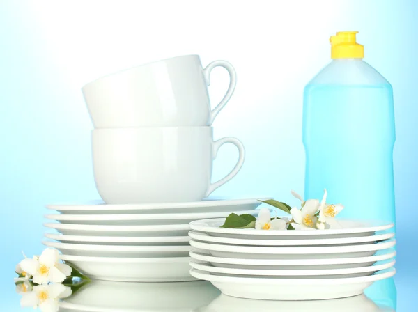 Lege schoon borden, kopjes en glazen met afwasmiddel en sponzen op blauwe achtergrond — Stockfoto