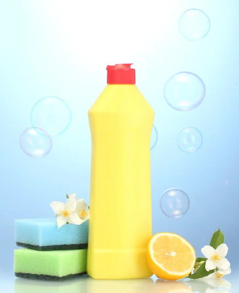Liquido per lavastoviglie con spugne e limone con fiori su sfondo blu — Foto Stock