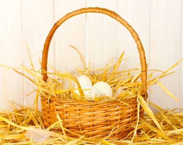Huevos blancos en una cesta de mimbre sobre paja sobre fondo de madera blanca —  Fotos de Stock
