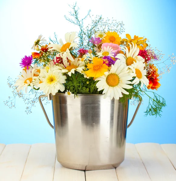 Schöner Strauß heller Wildblumen im Metalleimer, auf Holztisch auf blauem Hintergrund — Stockfoto