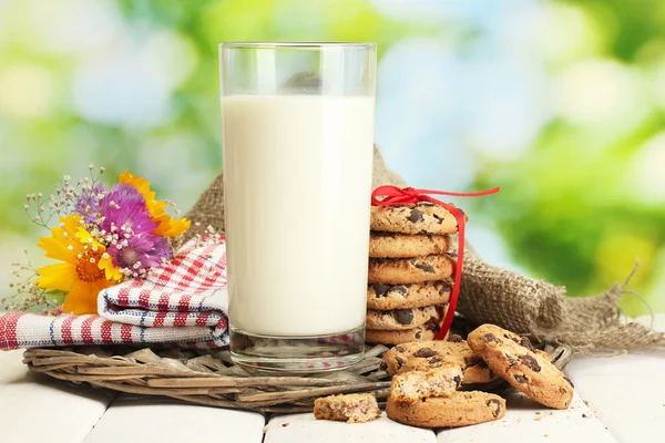 Vaso de leche, galletas de chocolate con cinta roja y flores silvestres sobre mesa de madera sobre fondo verde —  Fotos de Stock
