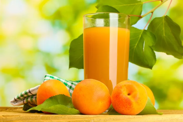 Glas aprikos juice och färska aprikoser på träbord på grön bakgrund — Stockfoto
