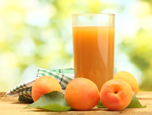 Стакан абрикосового сока и свежие абрикосы на деревянном столе на зеленом фоне — стоковое фото