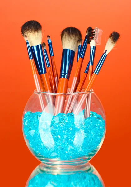 Make-up brushes in a bowl with stones on red background — Stock Photo, Image