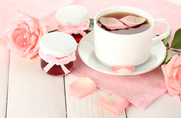 Kopje thee met rozen en jam op witte houten tafel — Stockfoto