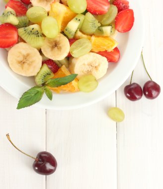 Fresh fruits salad on plate and berries on white wooden table clipart