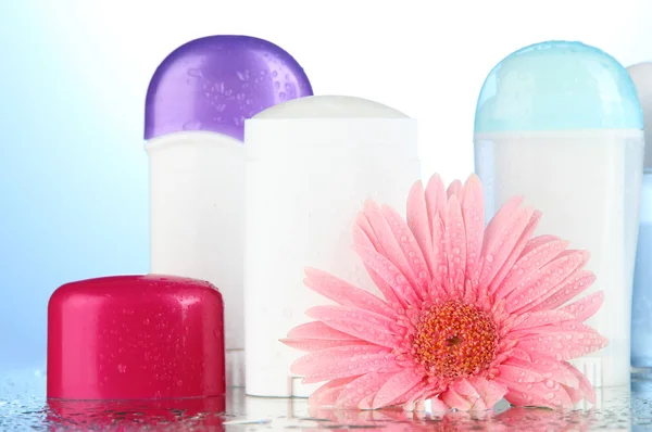 Garrafas desodorantes com flor no fundo azul — Fotografia de Stock