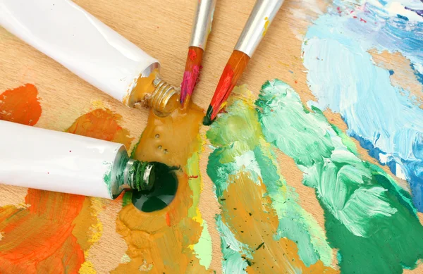 Abstract acrylic paint, paint tubes and brushes on wooden palette — Stock Photo, Image