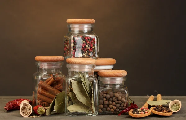 Burkar och skedar med kryddor på träbord på brun bakgrund — Stockfoto