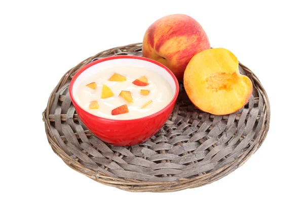 Yoghurt with peach in bowl on wicker mat isolated on white — Stock Photo, Image