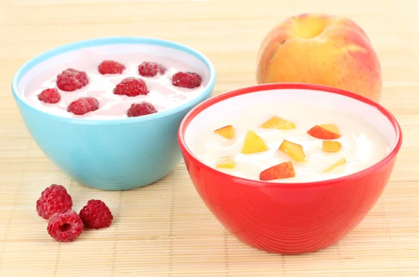 Йогурт с персиками и малиной в мисках на бамбуковом коврике — стоковое фото
