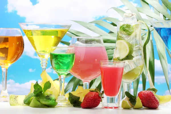 Glasses of cocktails on table on blue sky background — Stock Photo, Image