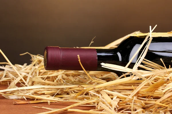 Пляшка великого вина на сіні на дерев'яному столі на коричневому фоні — стокове фото