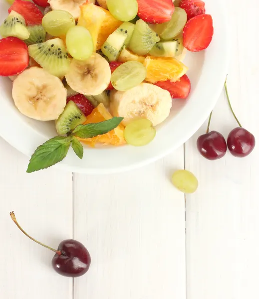 Ensalada de frutas frescas en plato y bayas en mesa de madera blanca — Foto de Stock