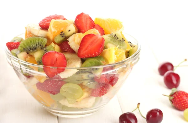 Glass bowl with fresh fruits salad and berries on white wooden table — Stock Photo, Image
