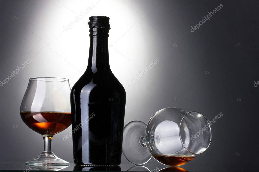 Glasses of brandy and bottle on gray background