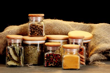 Jars with spices on wooden table on black background clipart