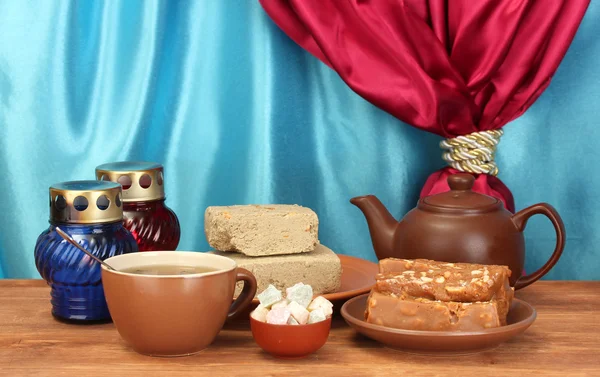 Bule com xícara e pires com doces orientais - sherbet, halva e prazer turco em mesa de madeira em um fundo de close-up cortina — Fotografia de Stock