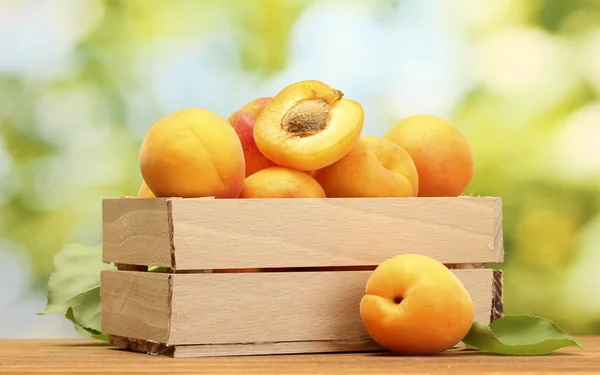 Rijpe abrikozen met bladeren in houten doos op houten tafel op groene achtergrond — Stockfoto